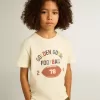 T-shirt da bambino in bianco consumato con scritte multicolori